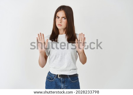Portrait of a serious young woman standing with outstretched hand showing stop gesture isolated over white background, strongly refuse and saying no Royalty-Free Stock Photo #2028233798