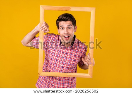 Photo of cheerful young amazed man hold hands wooden frame creative isolated on yellow color background