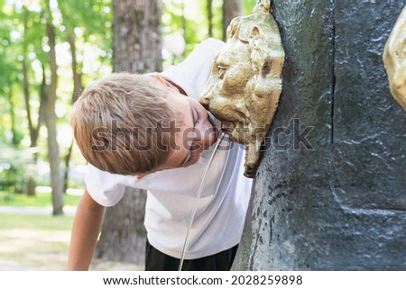 A little boy drinks water in a city park from a decorative column with lions