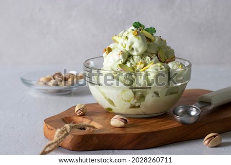Pistachio ice cream with nuts in transparent glass ice-cream bowl on a light gray background. Royalty-Free Stock Photo #2028260711