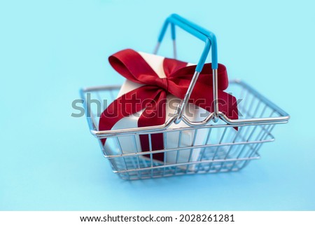 White gift box with red bow in supermarket basket on blue background