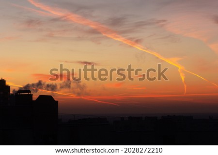 An urban silhouette with a colorful orange and red sky covered with contrails and clouds during sunrise and sunset.