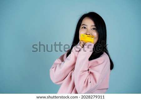 Portrait of an Asian girl wearing a pink shirt. in mobile credit card pose for a photo with a happy face Looking at the camera, behind a gray background in the studio.
