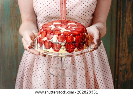 Woman holding strawberry cake on cake stand Royalty-Free Stock Photo #202828351