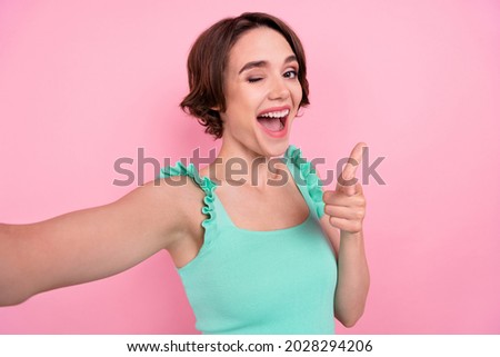Self-portrait of attractive cheerful funky girl winking pointing at you having fun isolated over pink pastel color background