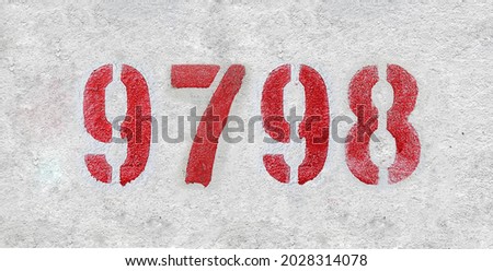 Red Number 9798 on the white wall. Spray paint. Number nine thousand seven hundred ninety eight.