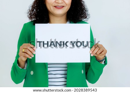 Studio shot of unrecognizable unidentified faceless female officer in business clothes holding thank you paper sign at chest showing appreciation to customers and colleagues on white background.