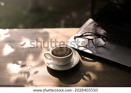 Hot coffee cup with laptop computer and eye glasses on wood table on morning summer. relaxation concept
