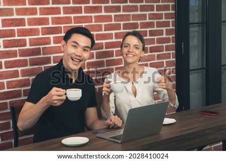 young Asian man and caucasian woman Happy smiling drinking coffee in cafe. People freelance holding latte cup Talking have fun laughing shopping online on laptop. background orange brick wall vintage.