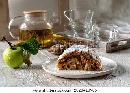 Strudel with apples and green tea on a wooden background. Homemade baking. Vertical photo. Selective focus. Tea table setting.