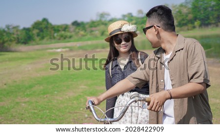 happy young asian couple walking bicycle in park in summer