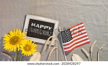 Happy Thanksgiving text on blackboard. Banner with USA flag, sunflowers, wheat ears, seasonal flowers. American Fall harvest festival. Flat lay, top view on beige textile .
