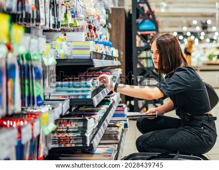 Portrait of young woman choosing school stationery in supermarket. Royalty-Free Stock Photo #2028439745