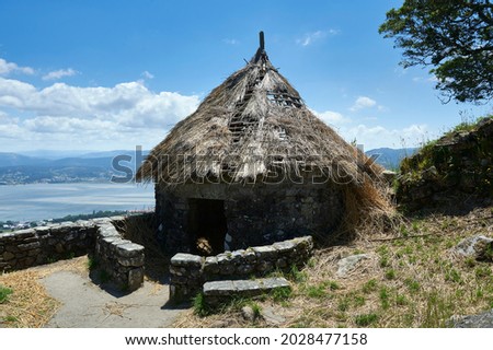 Stone walls and thatched roof of a house in the Celtic fort of Mount Santa Trega with the mouth of the river Miño in the background