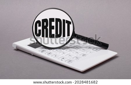 On gray background black calculator and magnifier with text CREDIT. Business concept