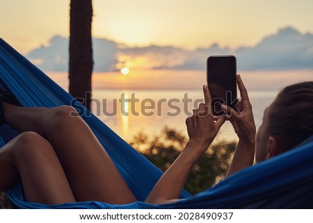 Woman in hammock taking a photo on smartphone