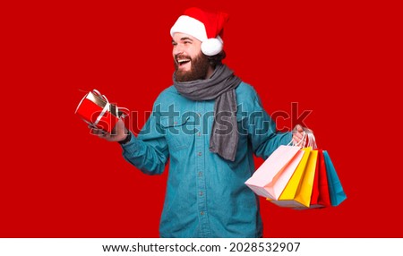 Just made my Christmas shopping, presents for all with some good discount. Happy man holding a gift box and some bags over red background.