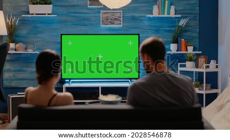 Caucasian individuals using television for green screen sitting on couch in living room. People with chroma key for virtual layout and mockup isolated template. Copy space background