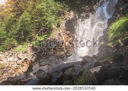 Attractive man standing in front of a big waterfall enjoying the amazing landscape views. Paradise mountain. Wild lifestyle relax, chill out and freedom. The beauty of nature concept.