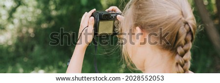 a happy little seven year old kid girl photographs a summer natural landscape with a camera using live view. children adopt their parents hobbies. summer children's education on vacation. banner