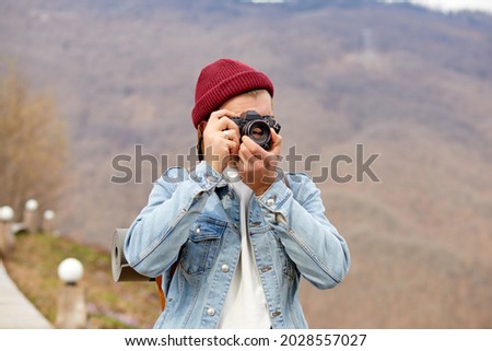 Young Man Traveler at vacations in mountains, take photo of nature. Lifestyle hiking concept. Portrait of hipster guy in denim jacket and hat using camera, enjoy traveling alone