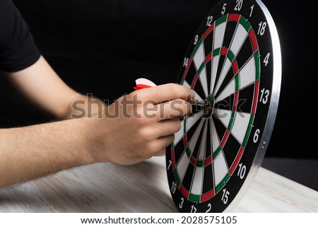Male hand and a dart board with a dart in the center on a black background in a low key. Goal achievement concept