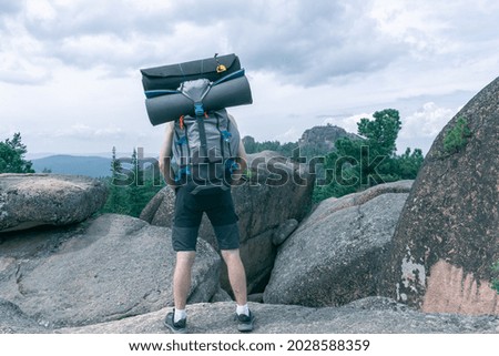 Back view of a guy with a backpack and camping equipment on the background of a beautiful landscape with rocks