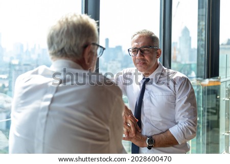 Picture of young business man taking to his older business partner. They are in white shirt and black tie. They are in a hotel lobby. 