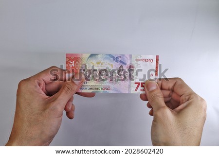 Male hand showing Indonesian rupiah note. Rupiah the official currency of Indonesia. Business and finance concept. Uang 75000 Rupiah. Bank Indonesia.  White Background. High Angle view. Flat Lay.