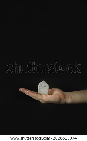 Hand holding mini house model on the black background. Buy or build a house. Concept for property ladder, mortgage and real estate investment. Free space for text, copy space, modern layout.