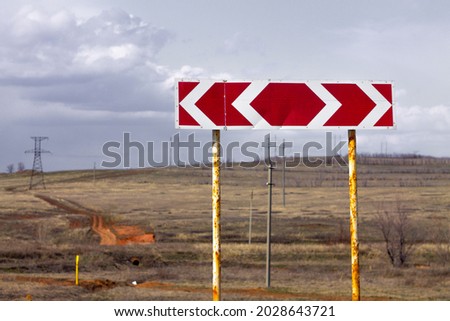 red road sign for the direction of turning on the background of the countryside, fields and roads