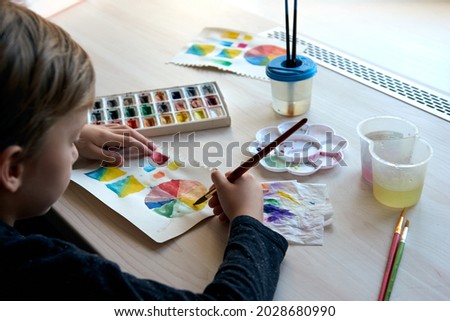 Boy painting pictures with watercolor paints during art lesson online