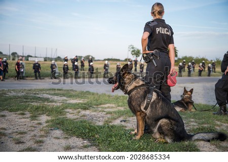 Police dog held by a policewoman (caption in Polish "Police") with many policemen in the background Royalty-Free Stock Photo #2028685334