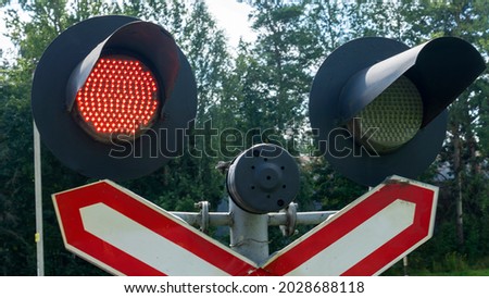 Road sign of railway crossing with double traffic light, shining red indicating approaching train. Close-up of an active railroad crossing light.