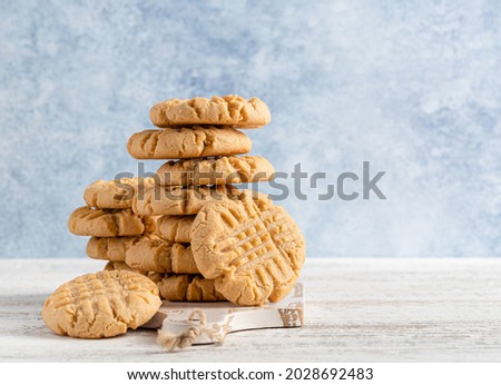 Peanut butter cookies stack on wooden cutting board. Traditional american dessert, nutrition snack, dessert or breakfast food. Blue and white background. Closeup food. Criss cross patterned biscuits. Royalty-Free Stock Photo #2028692483