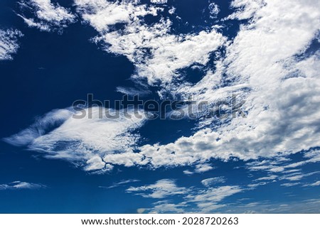Fluffy white clouds drift overhead, against the backdrop of a pale, blue sky.