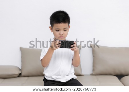 Little boy having fun playing game on mobile phone, Preschool kid sitting on sofa with smiling face watching cartoon on smartphone, Child using cell phone while relaxing at home