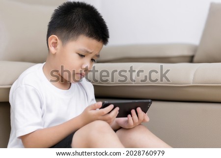 Little boy having fun playing game on mobile phone, Preschool kid sitting on sofa with smiling face watching cartoon on smartphone, Child using cell phone while relaxing at home
