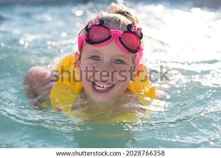 A happy girl in a yellow vest is swimming in the pool