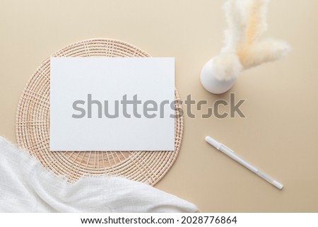 White invitation card, Blank Paper mockup on a beige background,  reeds grass in a vase, white blanket, Rattan basket, Flat lay, top view, copy space