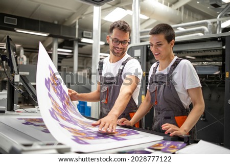 Graphic engineers or workers checking imprint quality in modern print shop. Royalty-Free Stock Photo #2028777122