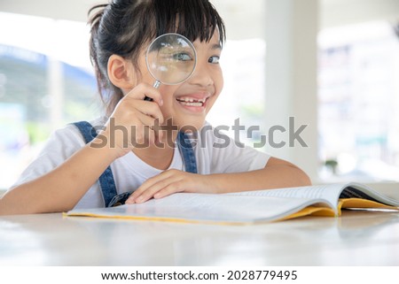 Asian Little girl reading the books on the desk with a magnifying glass