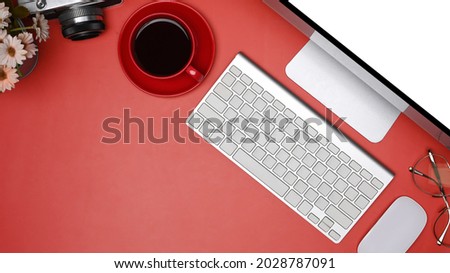 Modern workspace with computer, coffee cup and camera on red background.