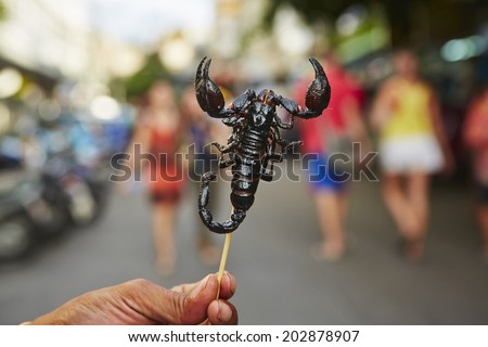 Hand of vendor with roasted scorpion. Street in Bangkok, Thailand.