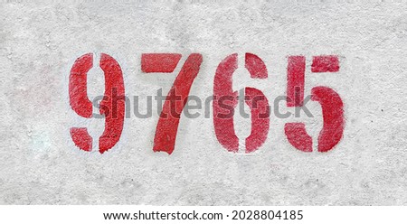 Red Number 9765 on the white wall. Spray paint. Number nine thousand seven hundred sixty five.