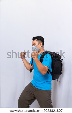 a man with black backpack wears medical mask and a cloth mask to protect from the covid-19 virus