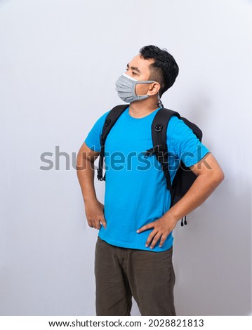 a man with black backpack wears medical mask and a cloth mask to protect from the covid-19 virus