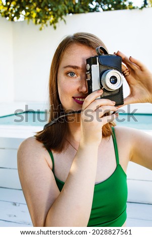 Portrait of young smiling woman taking pictures with retro camera outdoor in summer vacation.