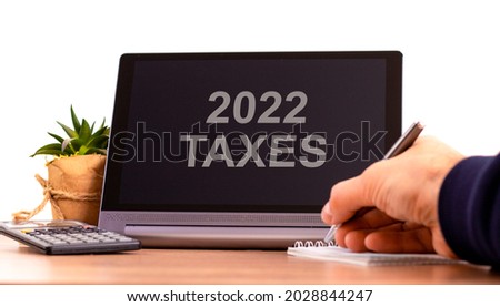 2022 taxes new year symbol. Tablet with words '2022 taxes'. Businessman hand with pen, house plant. Copy space. Beautiful white background. Business, 2022 taxes new year concept, copy space.
