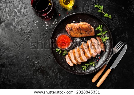 Roasted duck breast served with sauce and fresh herbs. Black background. top view